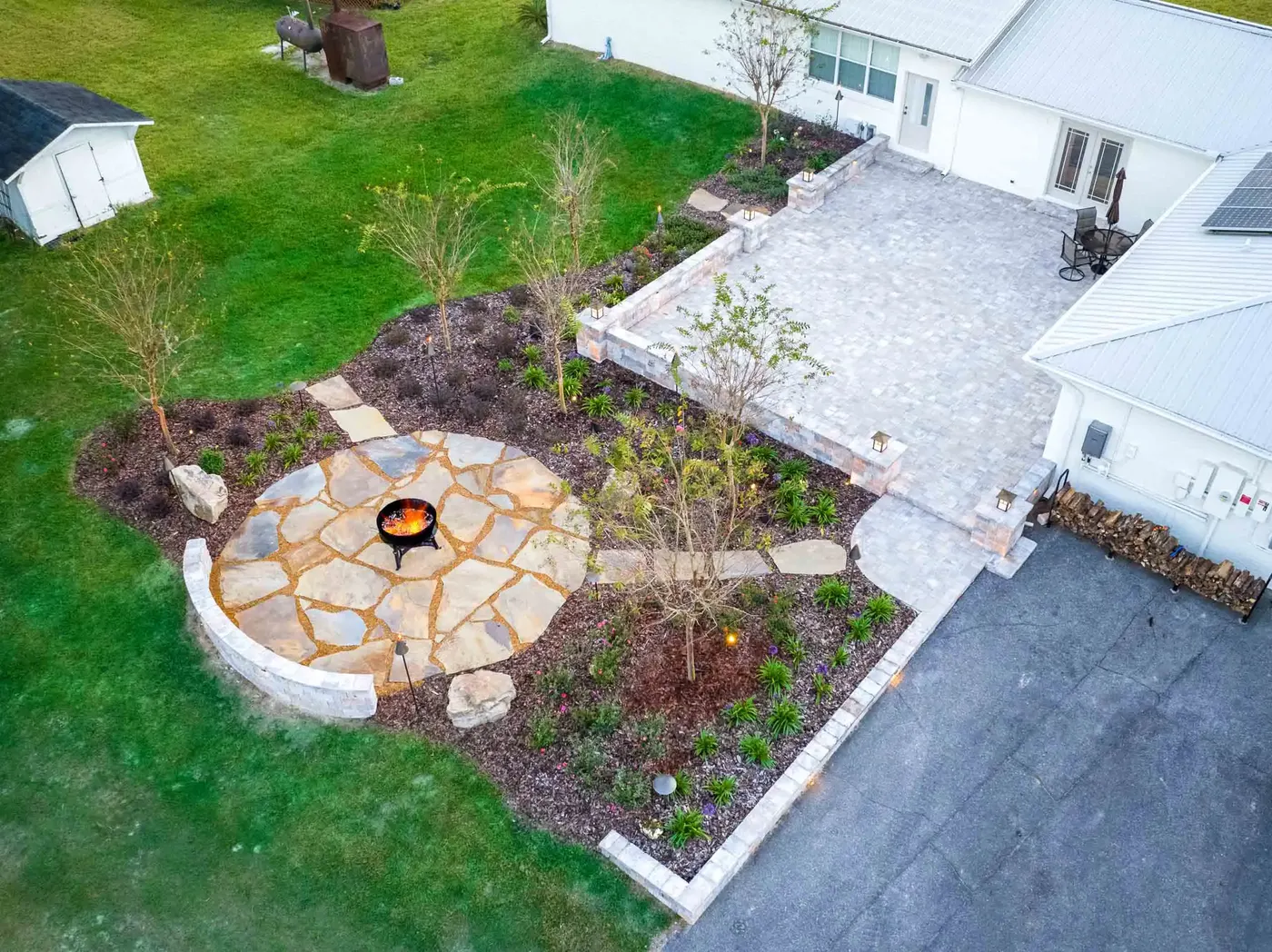 Drone view of a flagstone fire pit circle and paver patio beside a home