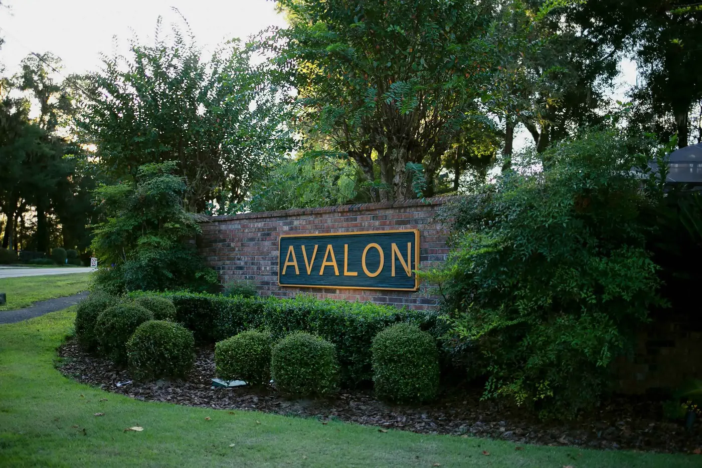 Neighborhood entrance sign framed by clipped shrubs and oaks