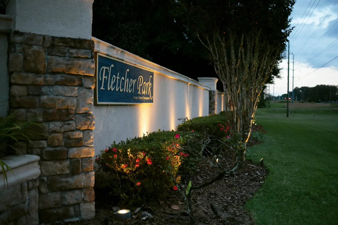 Stone entrance sign uplit with plantings at dusk
