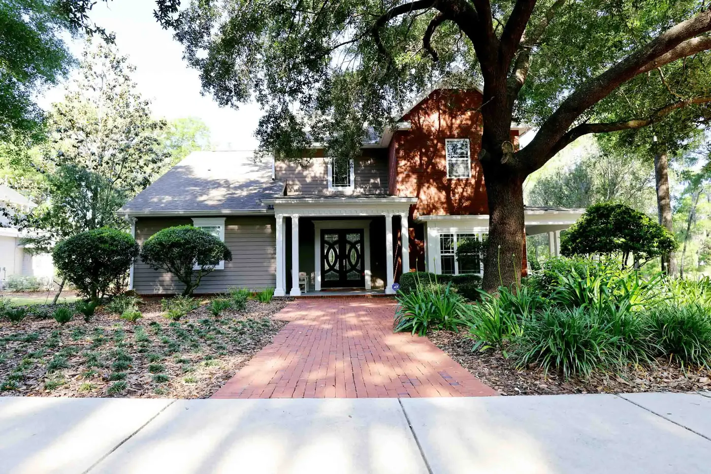 Home with a brick driveway under a live oak and new beds
