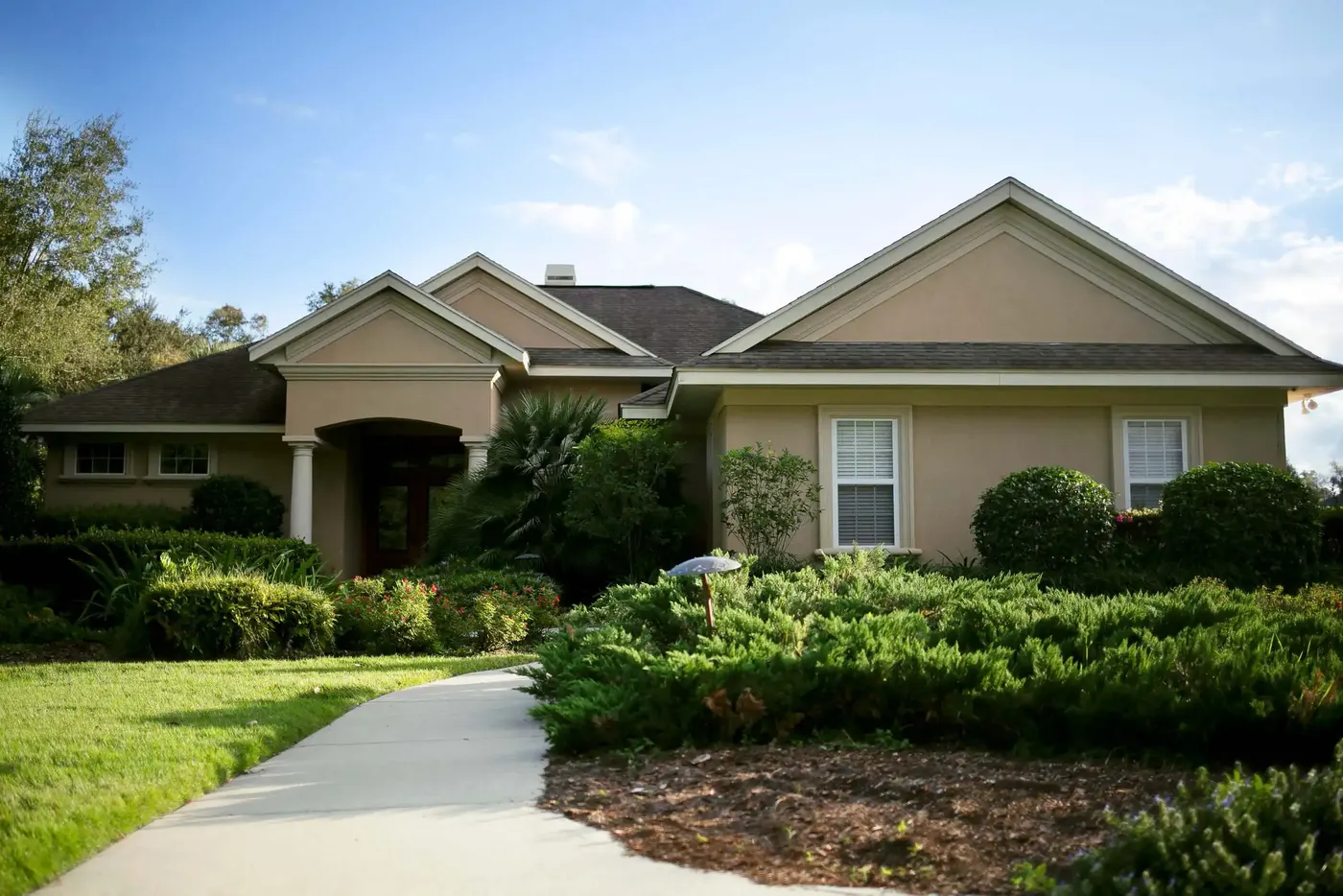 Stucco home with a walkway through layered shrub beds