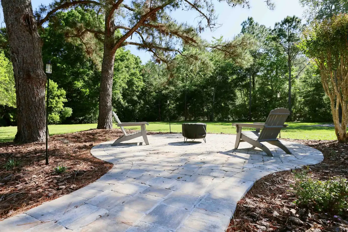 Paver patio with Adirondack chairs and a fire pit under live oaks