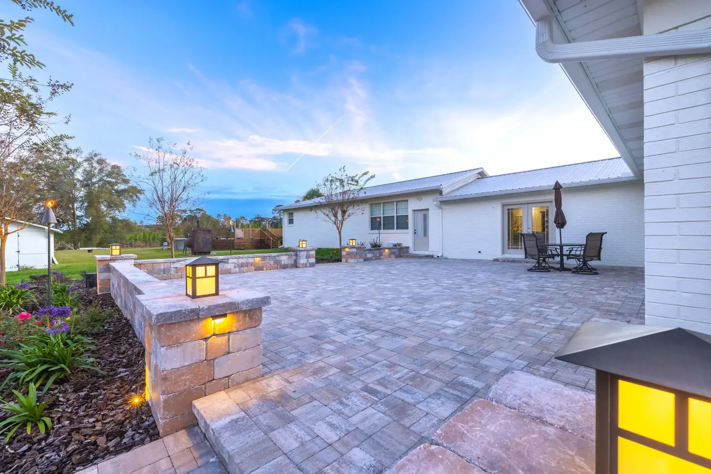 Paver patio with a lit column lantern and seating wall at blue hour