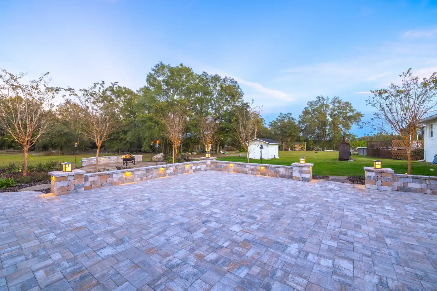 Wide paver patio with a curved seating wall lit at dusk