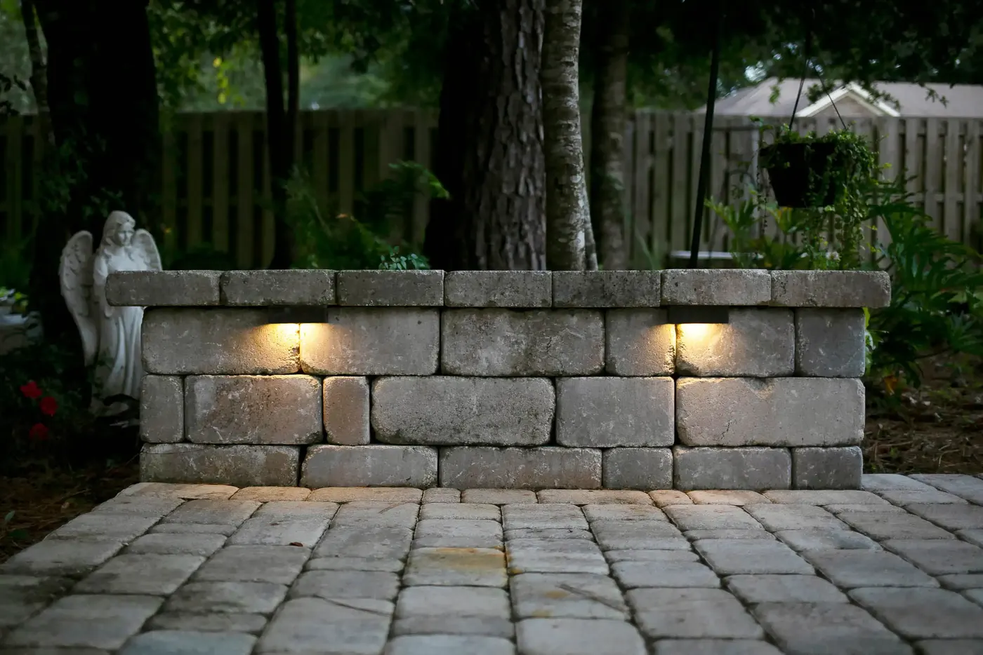 Lit stone seating wall with a garden statue at dusk