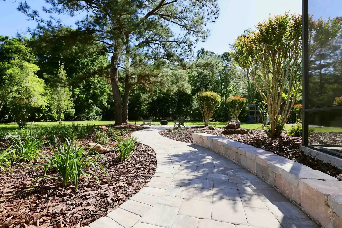 Curved paver walkway with a low seating wall through new beds